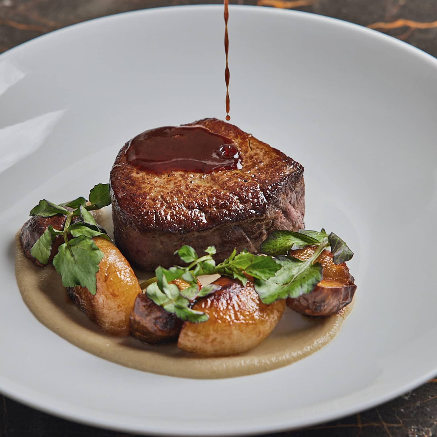 A filet of steak with potatoes and herbs on a white plate.
