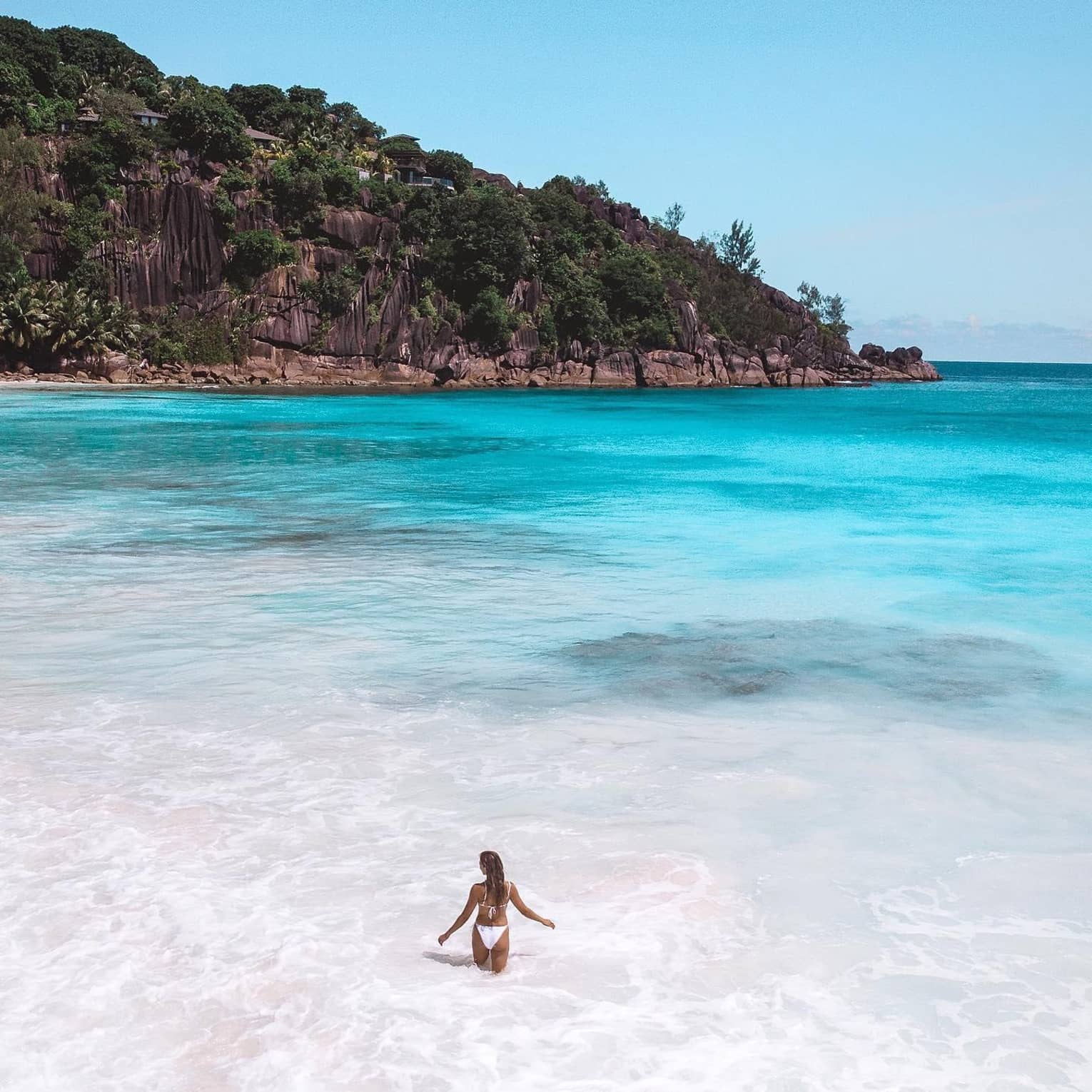 Woman wades in blue lagoon surrounded by tropical hills