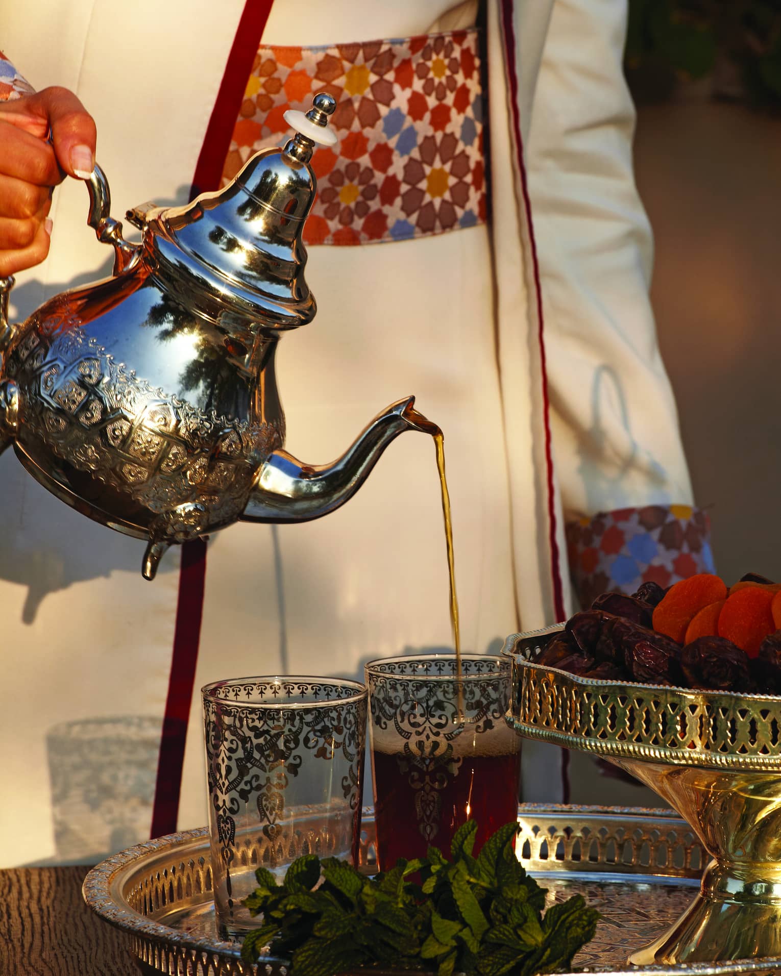 Small silver teapot pouring tea into decorative Moroccan glasses