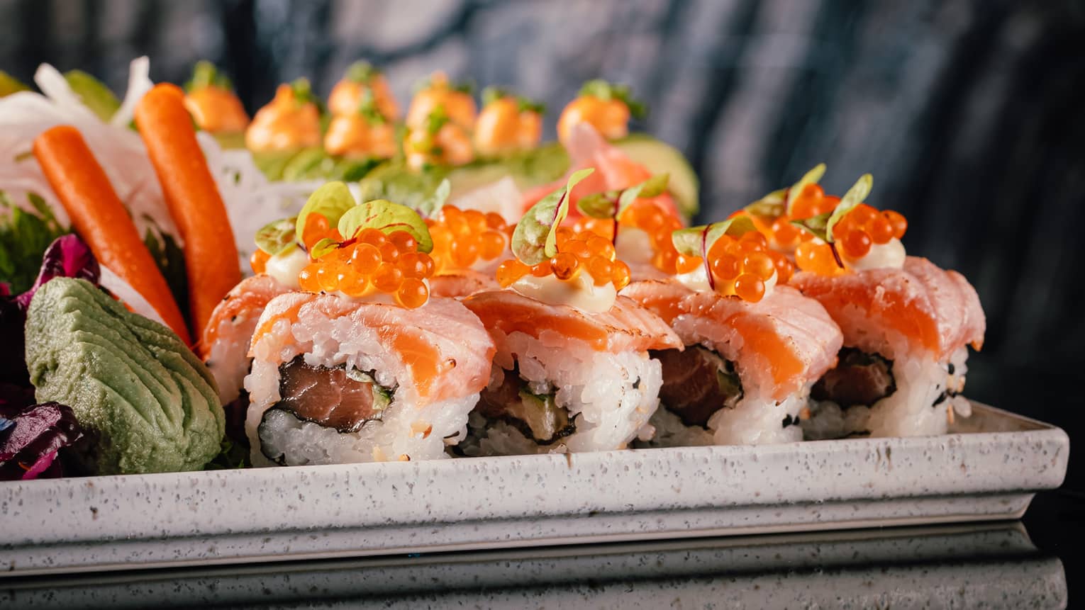 A platter of colorful sushi rolls set on a black mirrored table