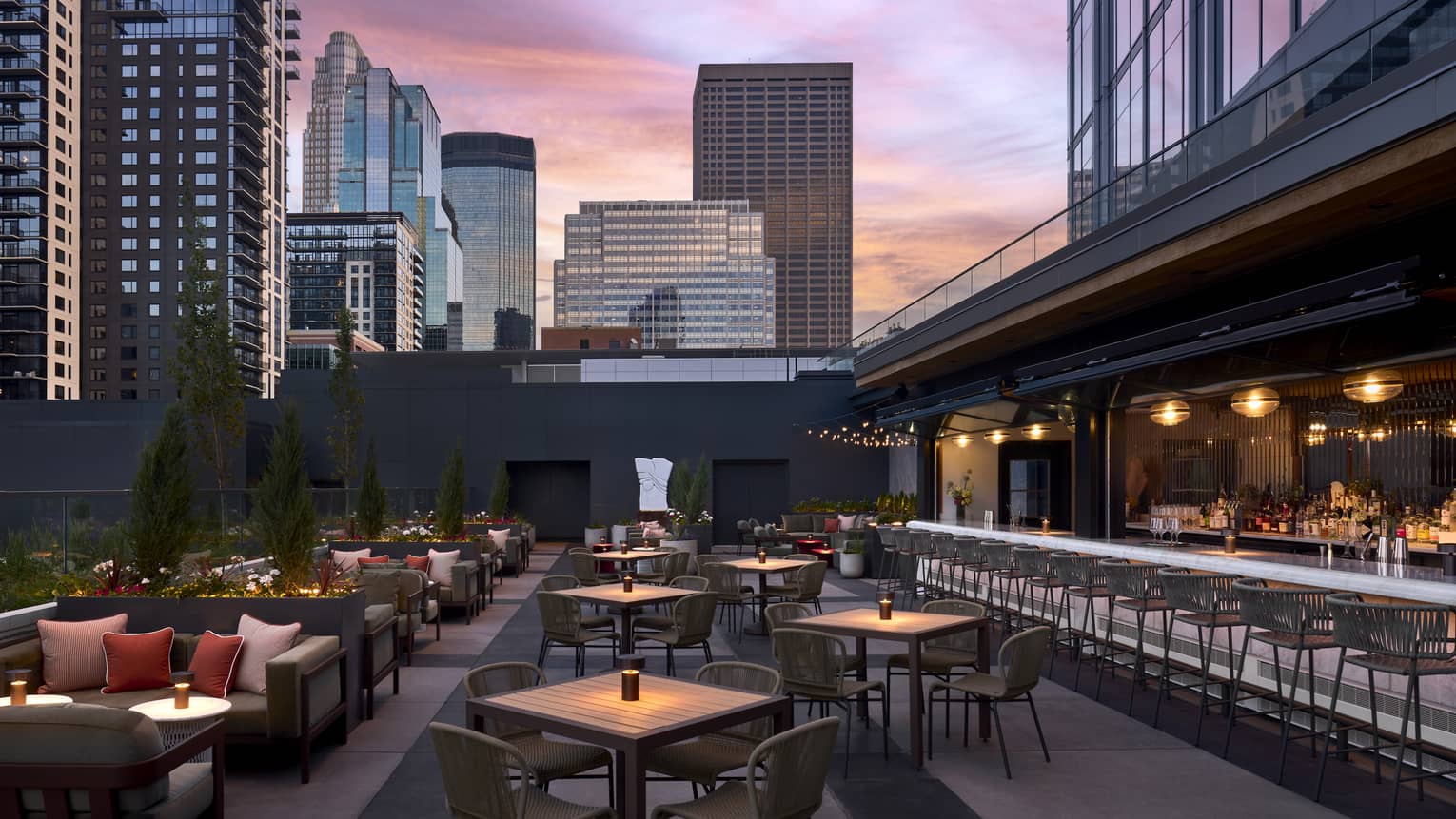 An outdoor plaza with sofas, tables, chairs and patio with a city in the background.