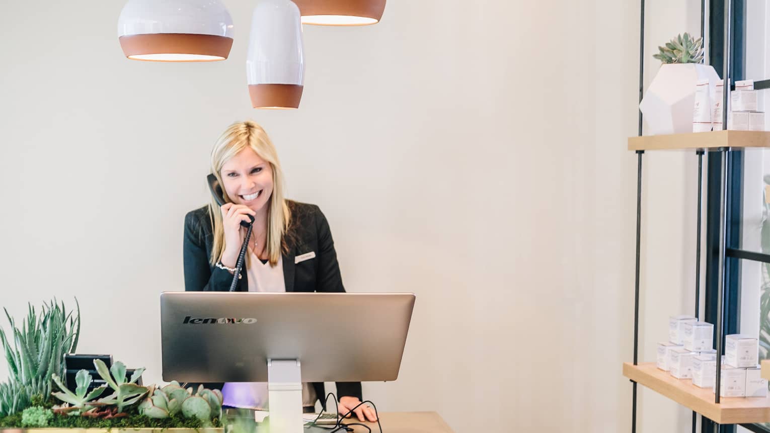 Smiling spa staff on telephone behind large silver computer screen