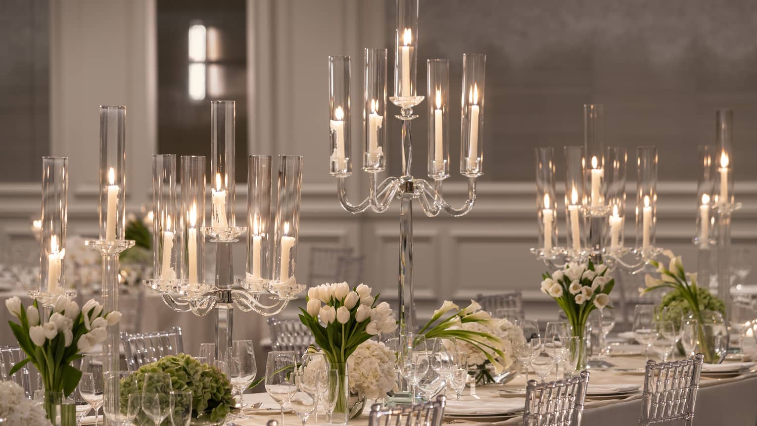 Formally set white dining table with candelabras and white flowers flanked by silver chairs