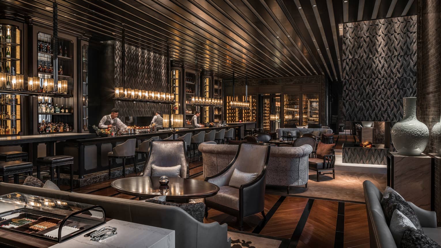 Gusto Bar bartenders at long bar lined with silver stools, grey velvet sofas, chairs