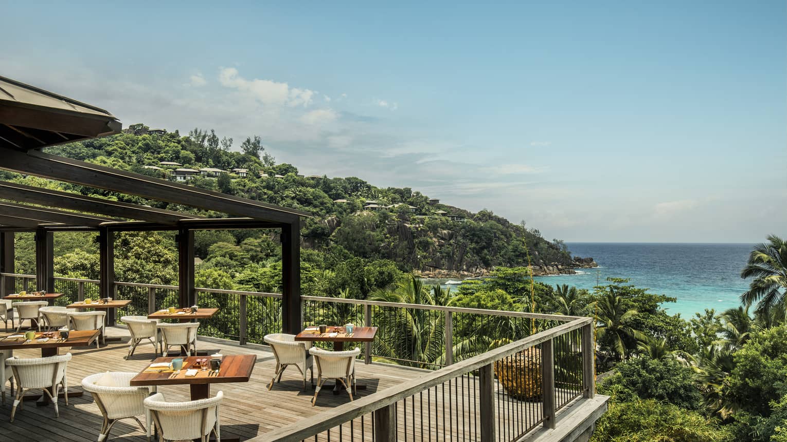 ZEZ outdoor dining room on wood deck overlooking palm trees, blue sky