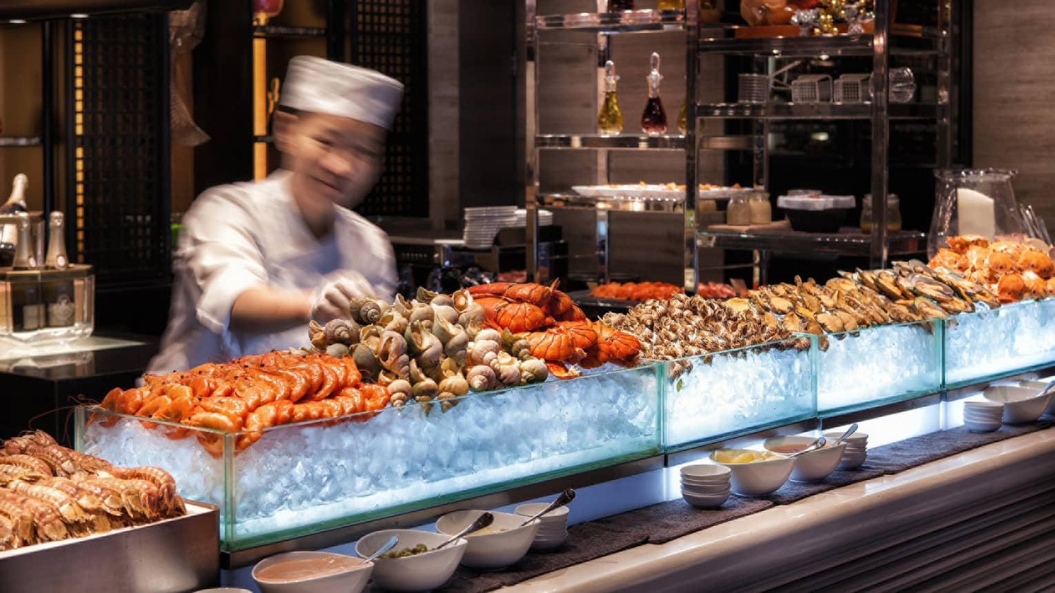 Chef reaches for snails on fresh seafood display on ice at bar