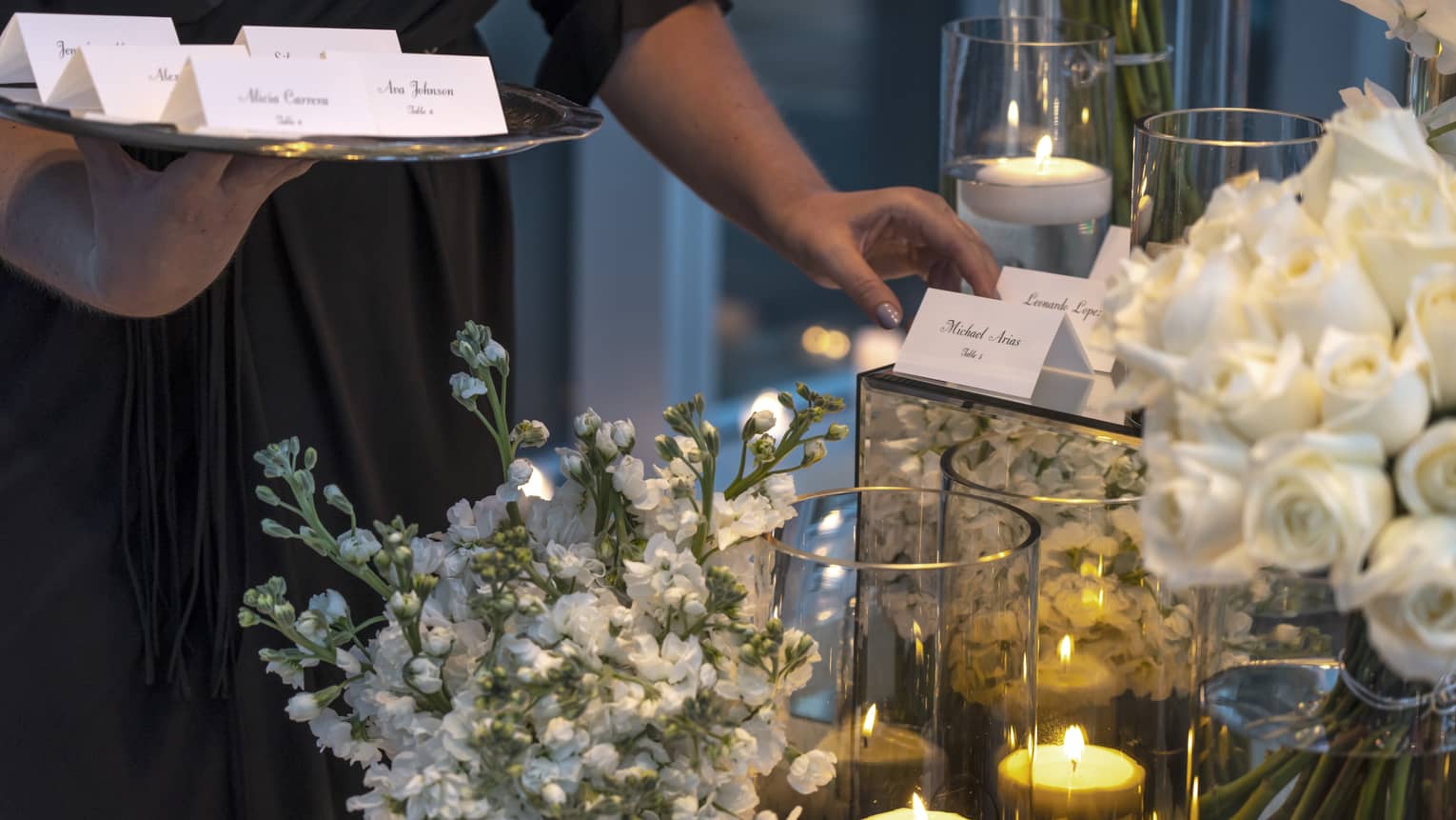 Event staff with tray places name cards on elegant banquet table with white flowers, candles
