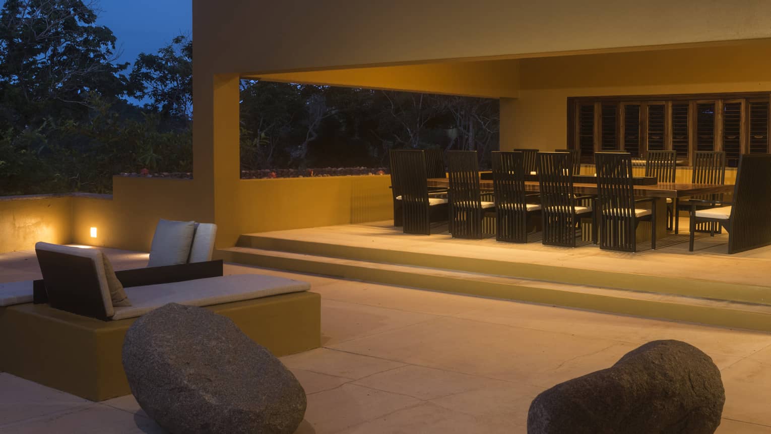 Exterior back terrace of private villa, with rock boulder seats and a large dining table