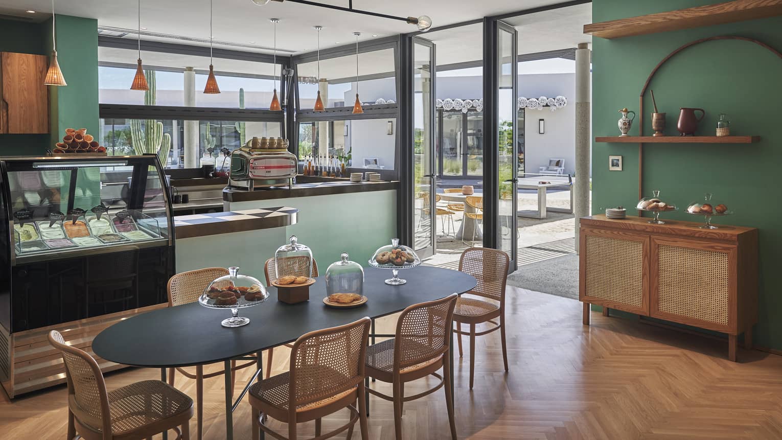 Green-walled Gingers dining area, black oval table and wicker chairs, food display case