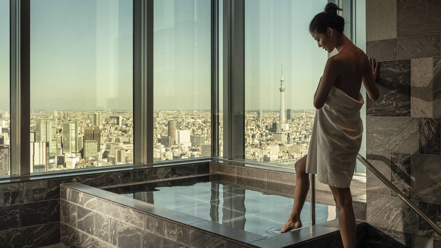 Woman wrapped in white towel dips her toe into the ofuro bath