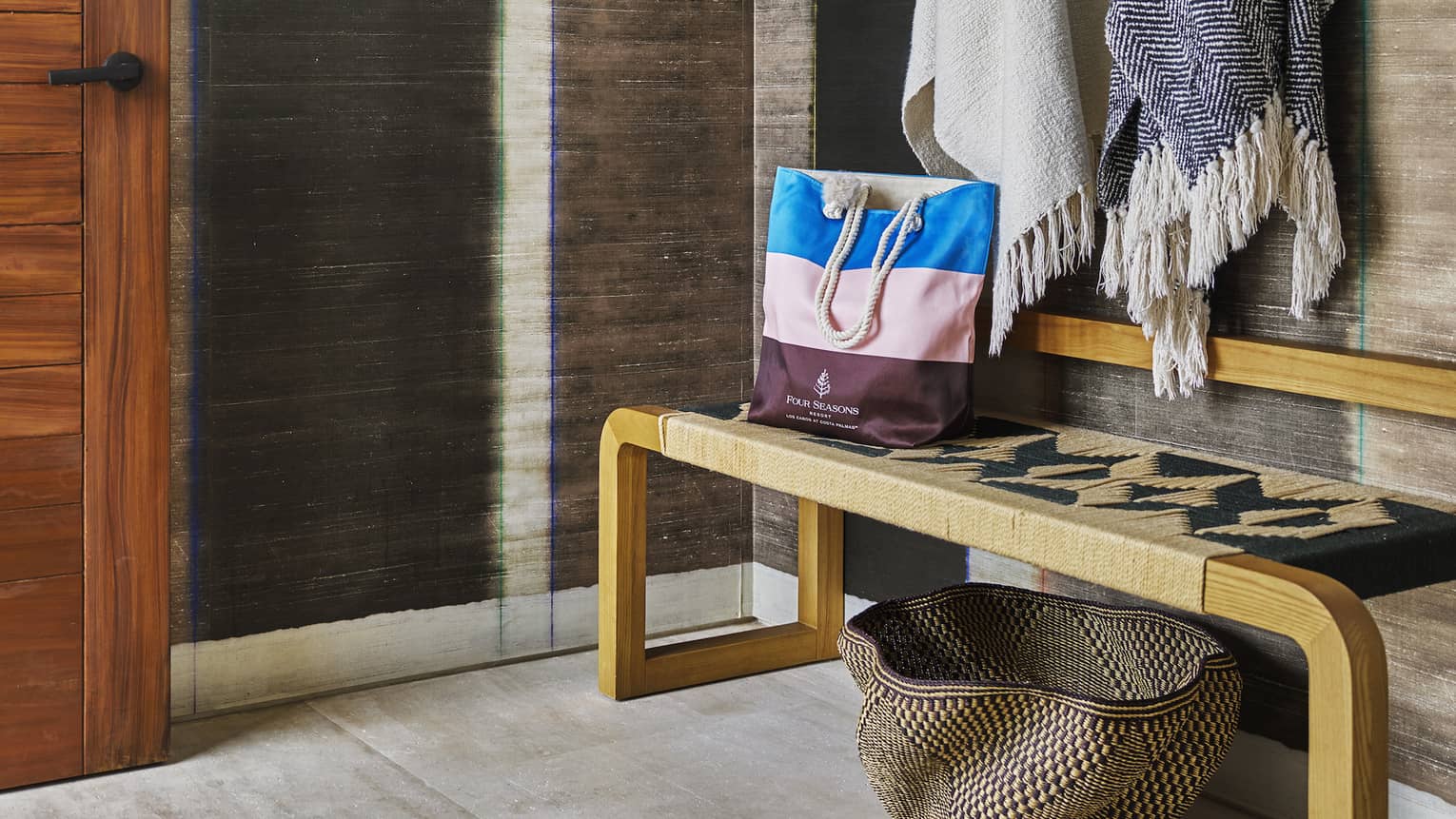 Resort room entryway with stylish wooden bench, shawls and hat hanging on wall hooks and a straw basket