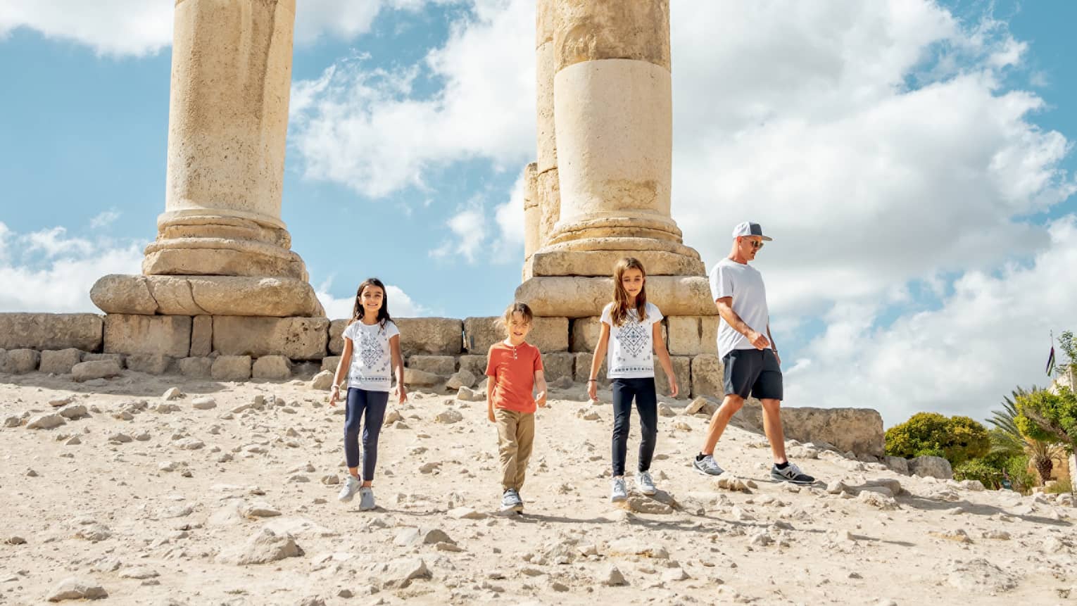 A parent and three children walk together next to the ruins of the Amman Citadel