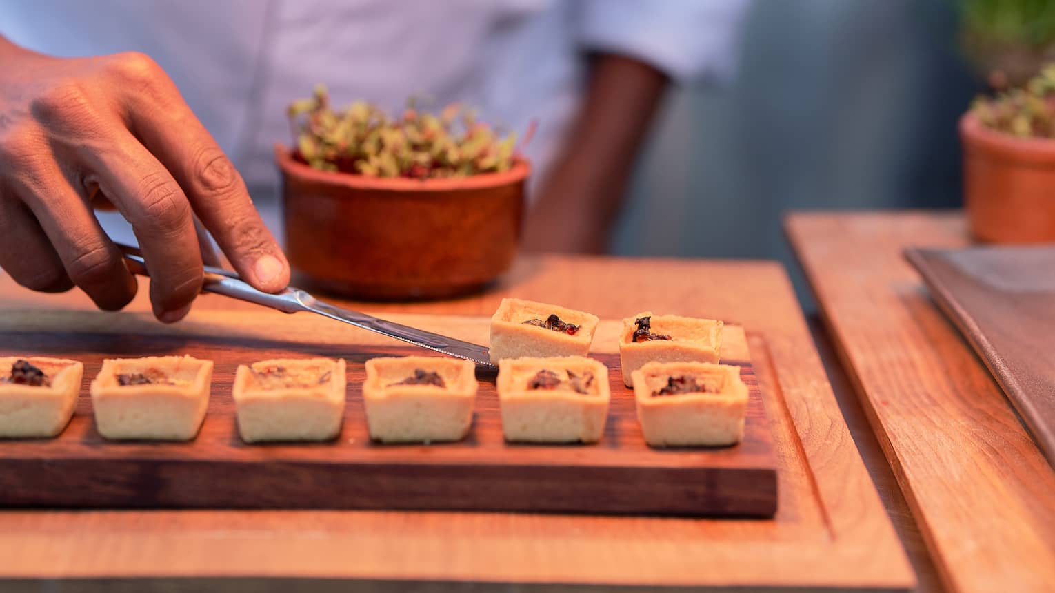 Chef puts finishing touches on small handheld appetizers on wooden serving board