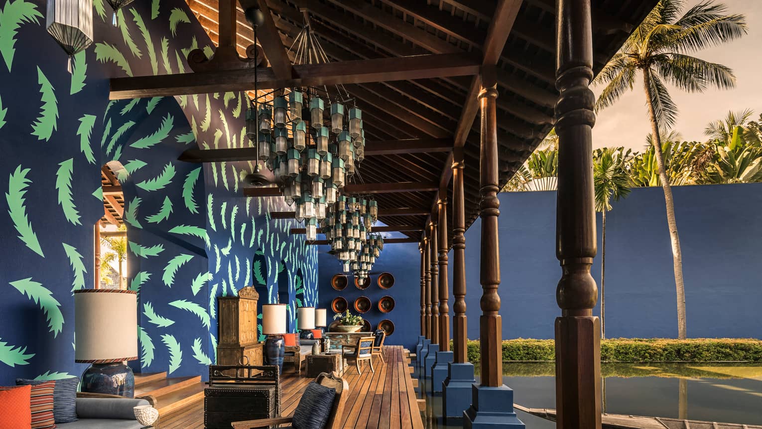 Bold blue and green palm print on wall, wood furniture, modern lantern chandelier