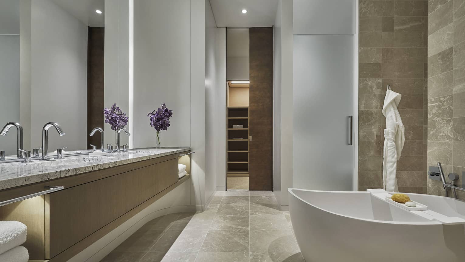 Beige marble bathroom with white free-standing tub, marble vanity, frosted glass shower