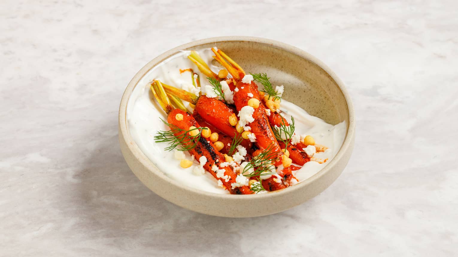 Grilled carrots served in a bowl with Greek yogurt, chickpea pops and dill