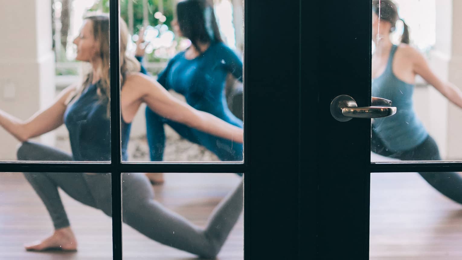 View through studio French doors to women stretching in yoga poses