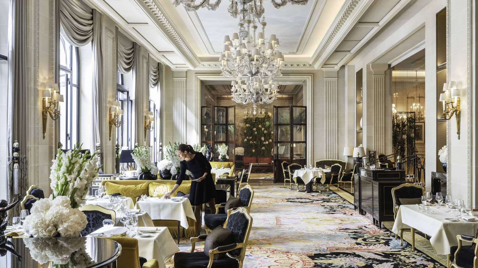Staff member setting table in formal dining area with Queen Anne chairs, chartreuse sofas, white floral arrangements and floor-to-ceiling windows