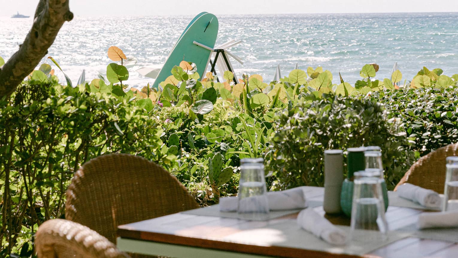 Outdoor dining table set beneath a green-and-white umbrella overlooking the ocean