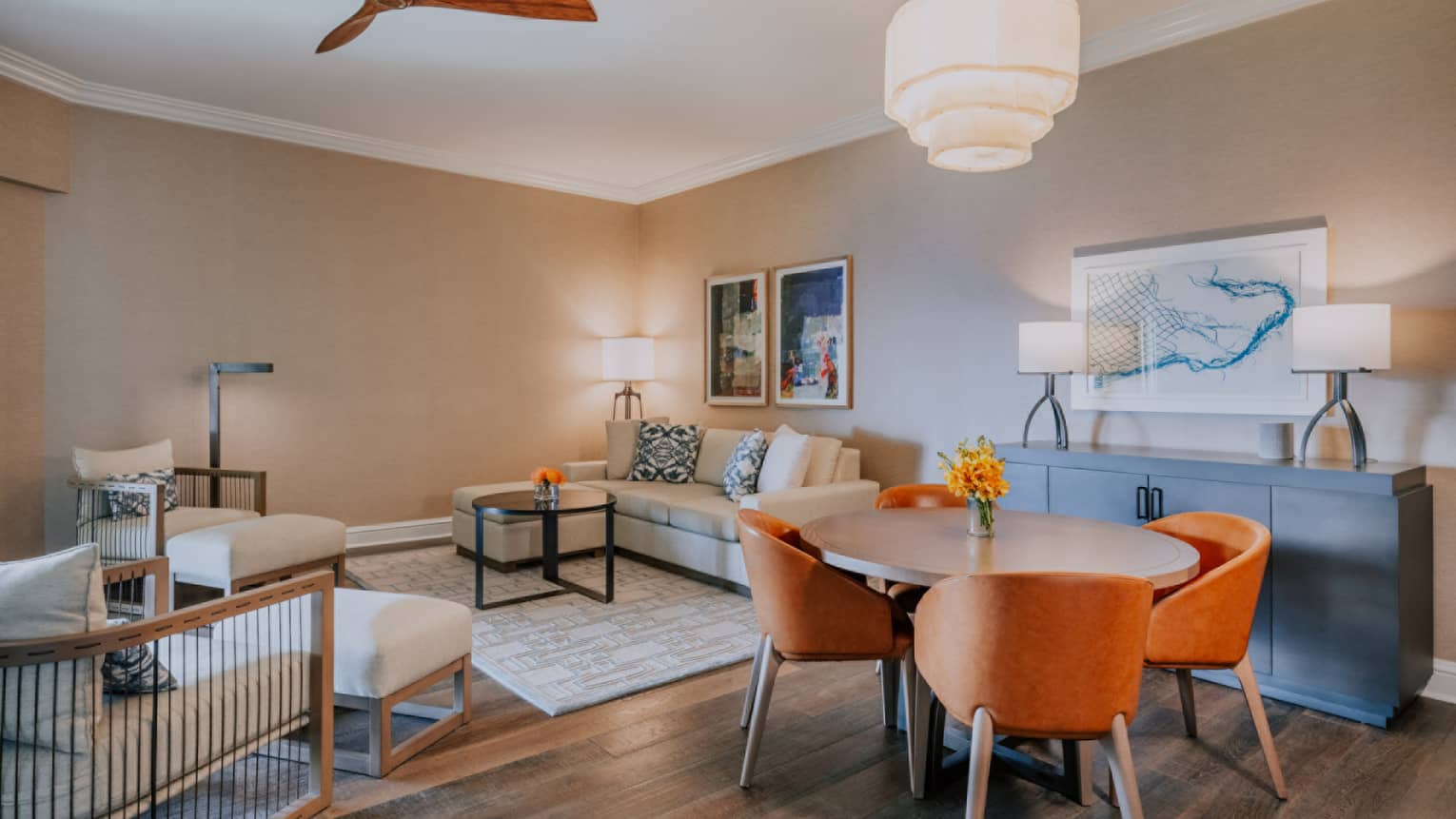Contemporary living and dining area with round table, orange chairs, beige sofa and modern artwork on neutral walls