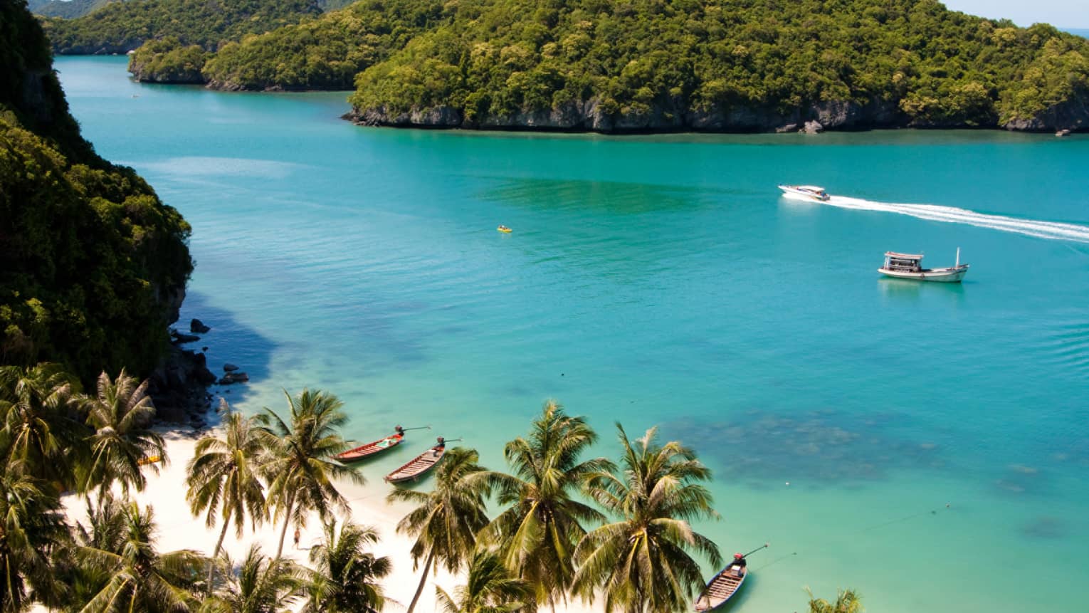 Boats traveling across peaceful blue water in Koh Samui, near a beach with palm trees