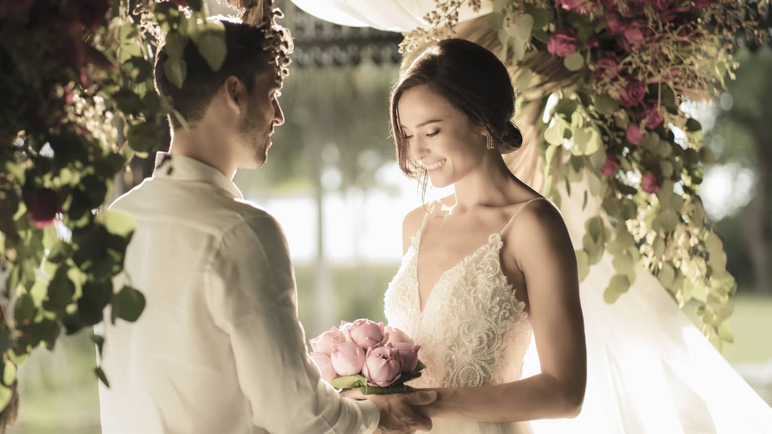 A man and woman are getting married under a pink and green floral arbor with tons of warm natural light