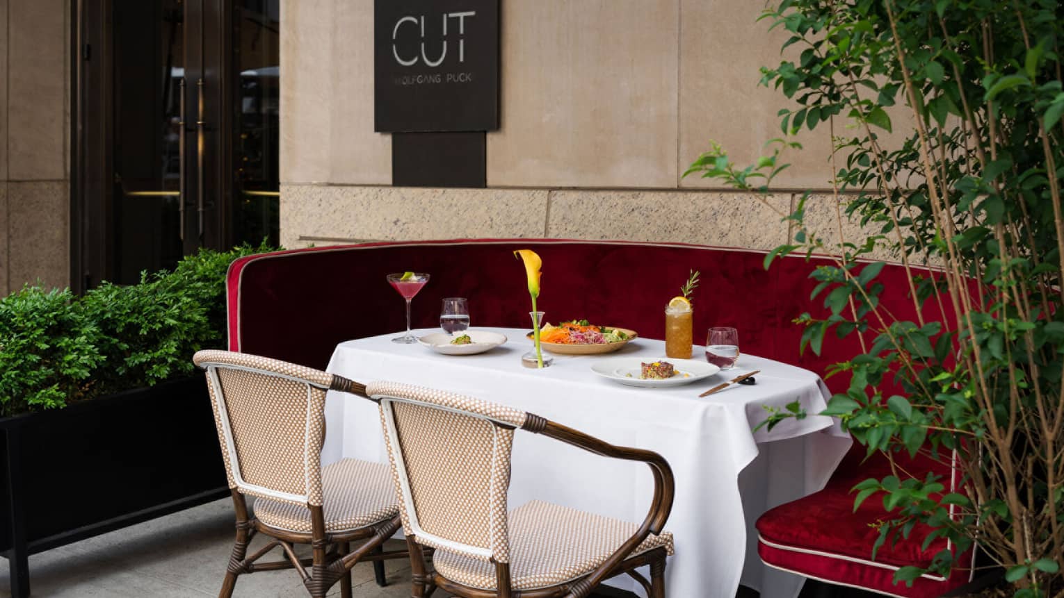 ,An outdoor table with two wooden chairs and a red velvet booth set with colorful food and beverages