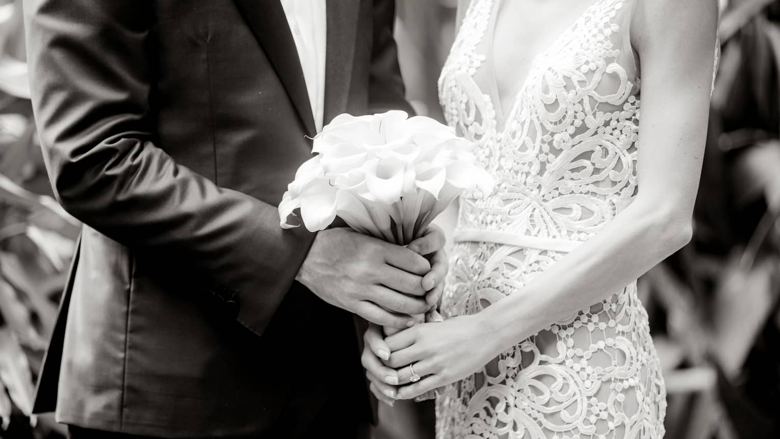 Black and white image of bride wearing lace dress, groom holding wedding bouquet