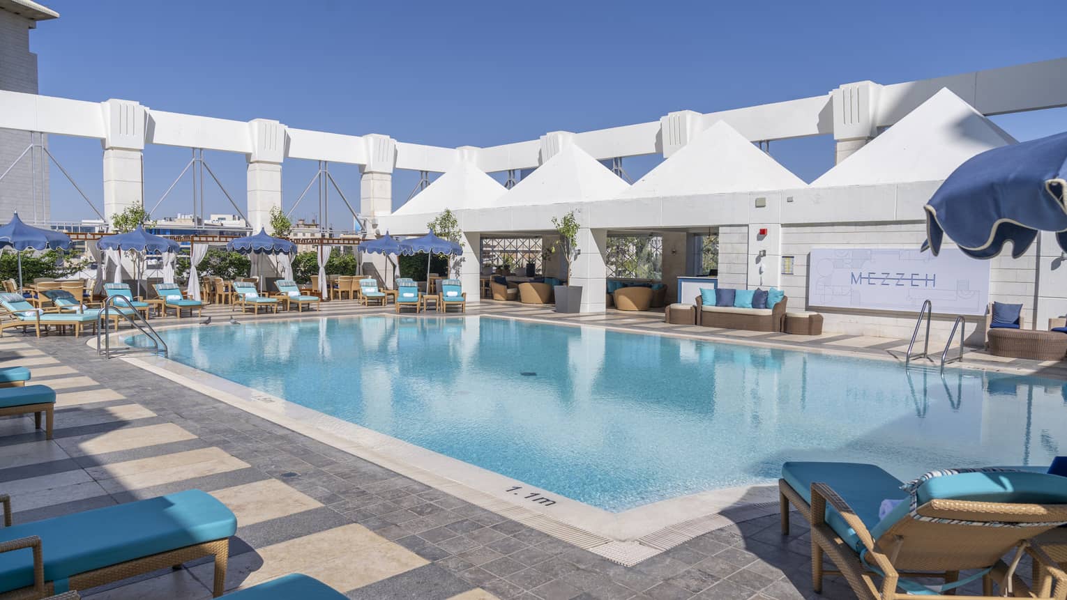 Outdoor pool surrounded by blue lounge chairs and four white tents