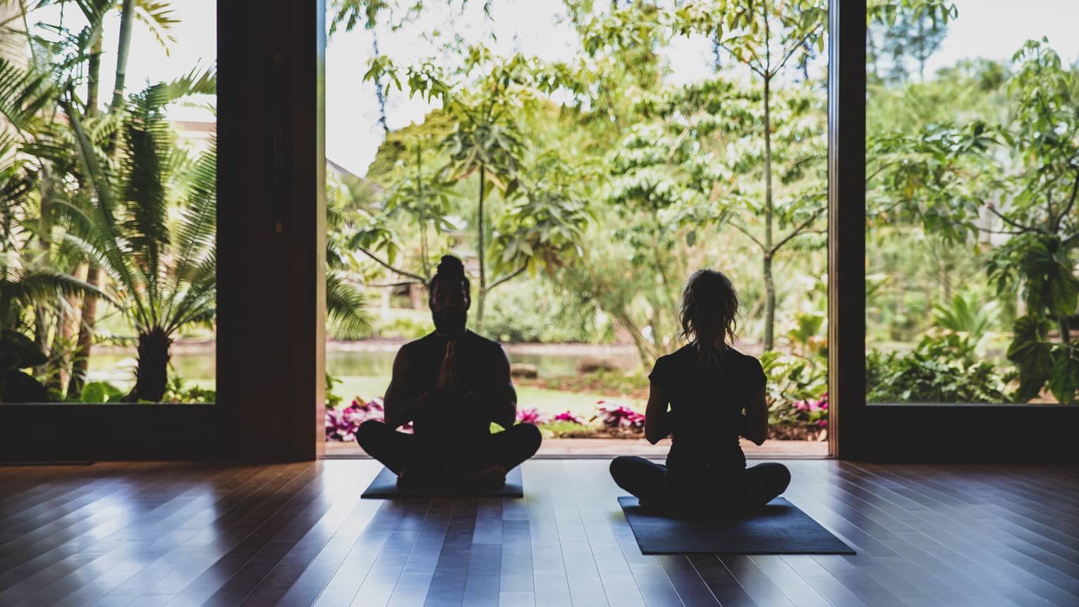 Two people practice yoga in the outdoor covered pavilion surrounded by greenery
