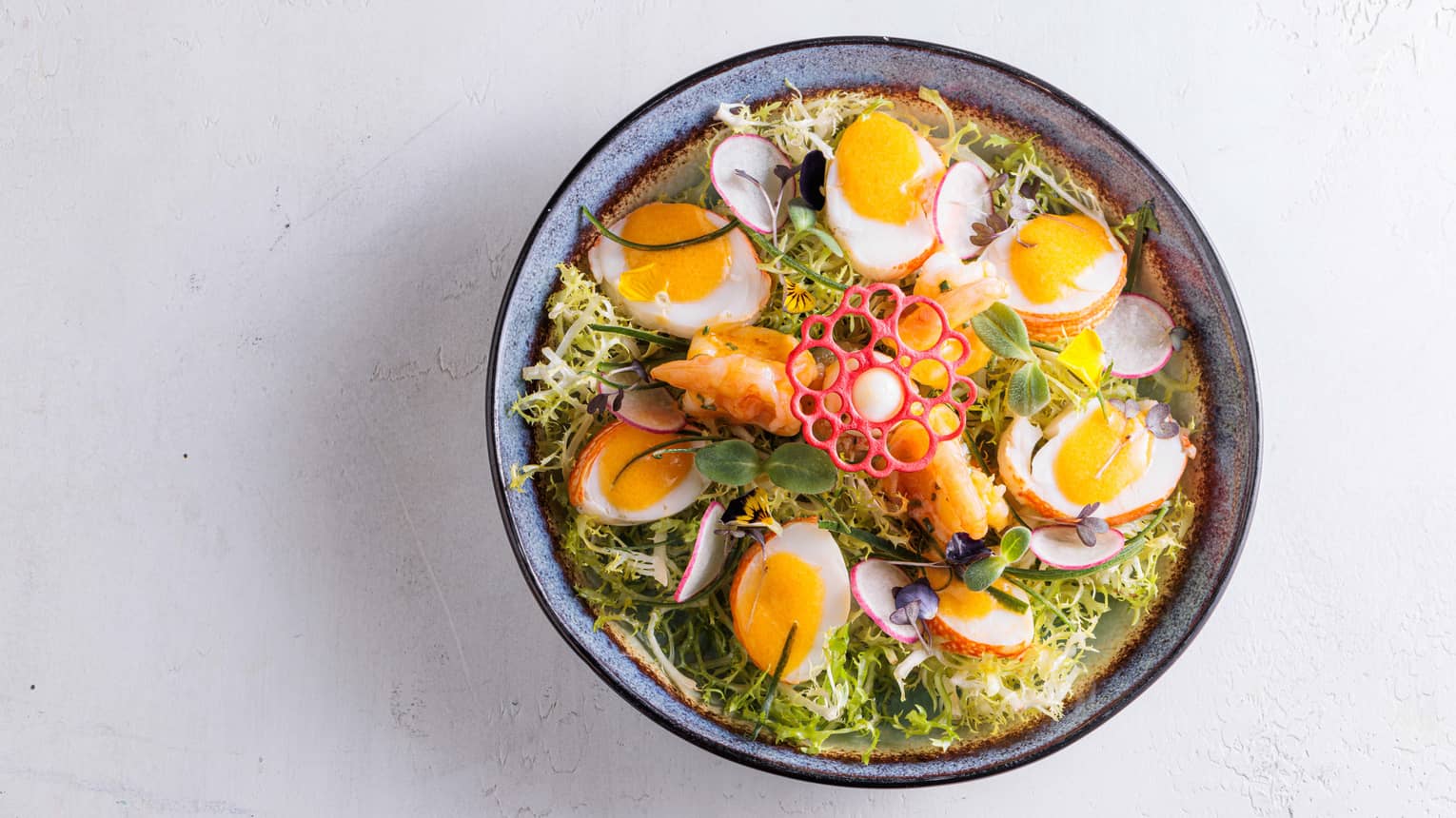 Bowl of greens, halved soft-boiled eggs, sliced radishes and a decorative garnish