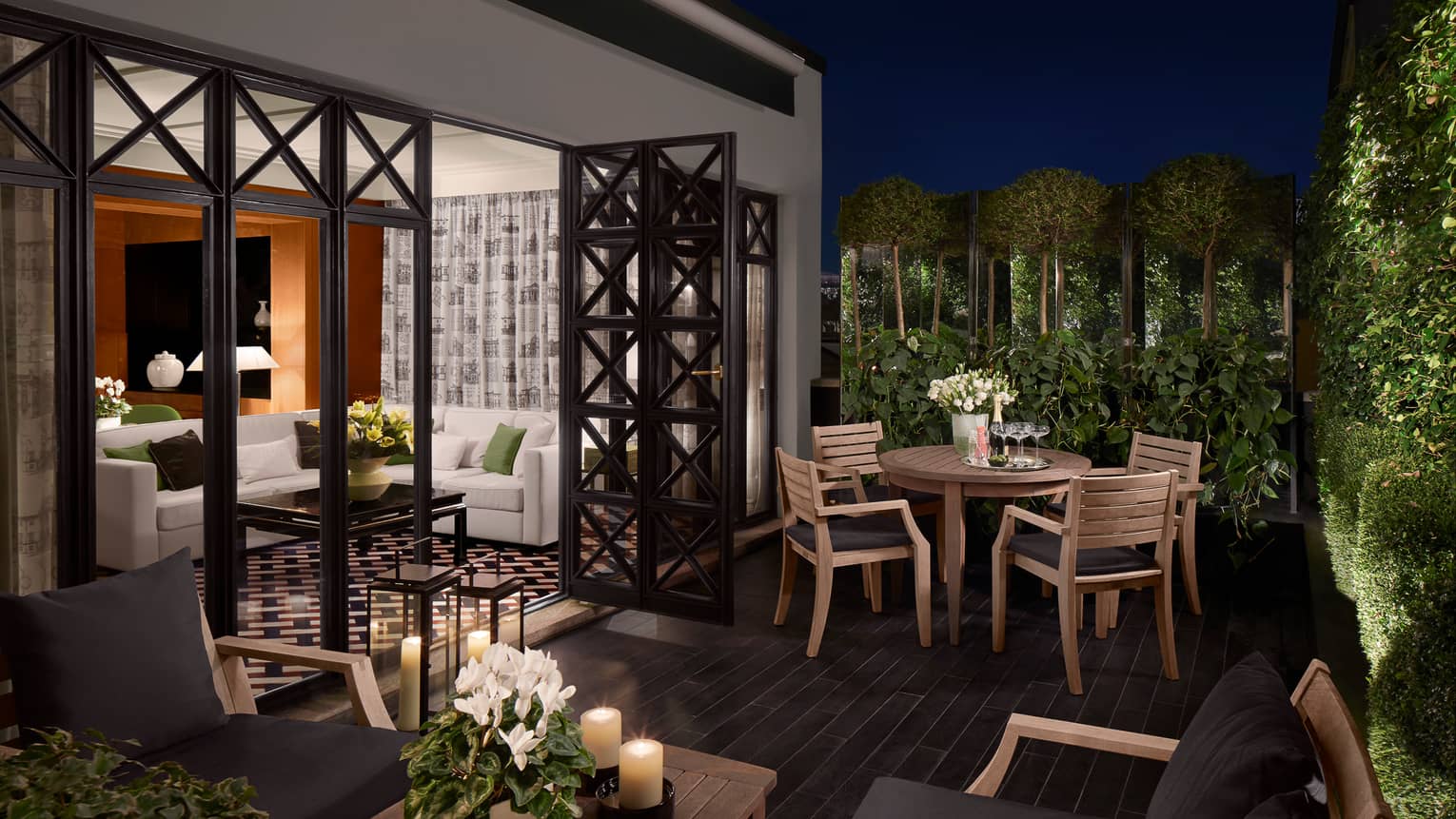 Balcony with wood tables and candles, chairs with black cushions, open doors to suite, white sofa