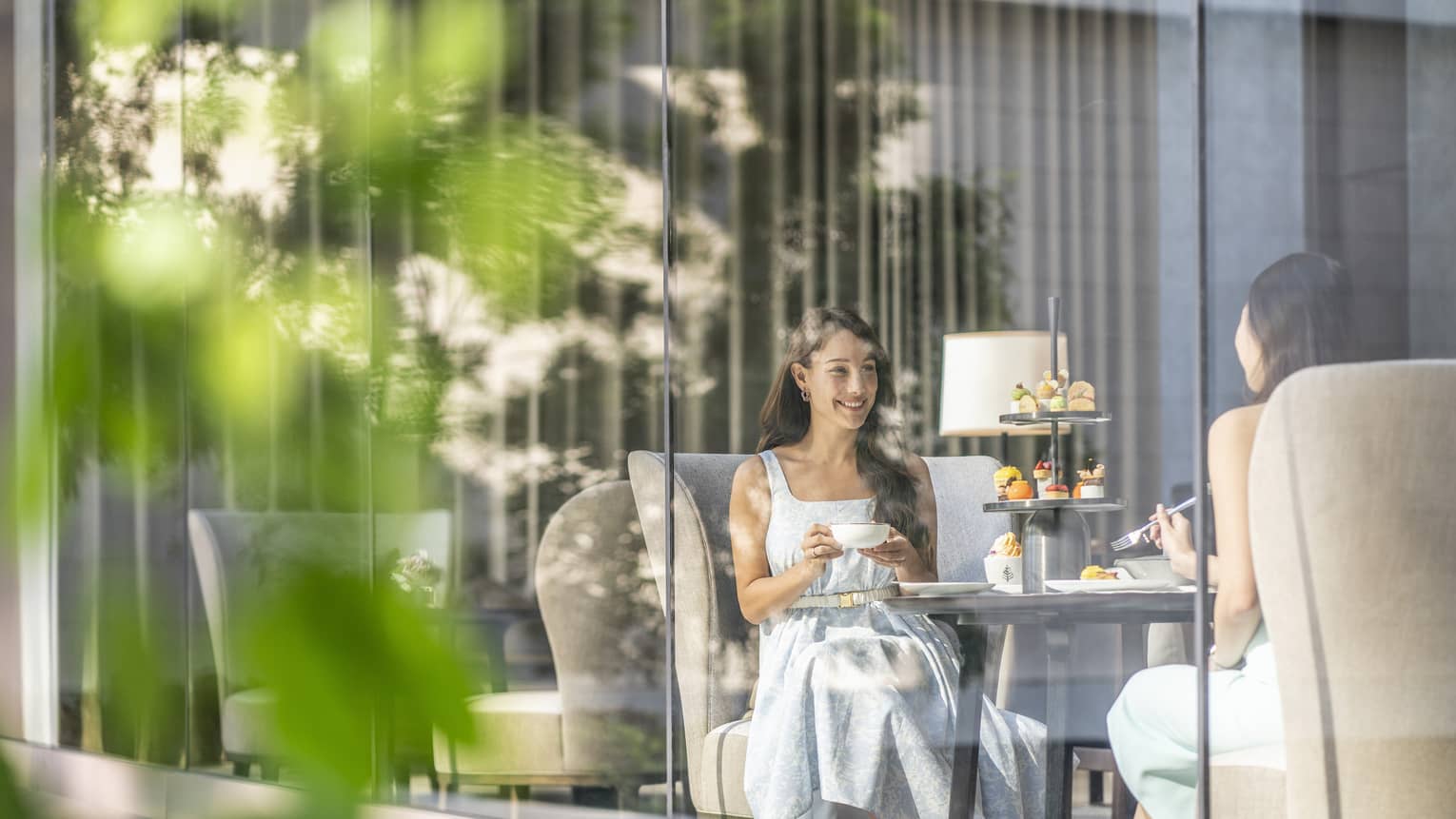 View through cafe glass window where two women enjoy afternoon tea and desserts