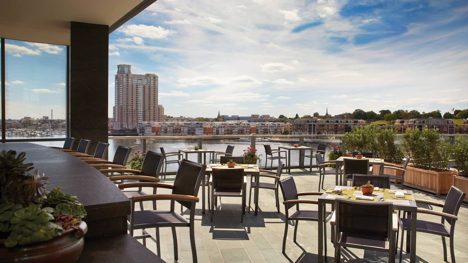 Bar with stools, tables and chairs on sunny patio with harbour view 