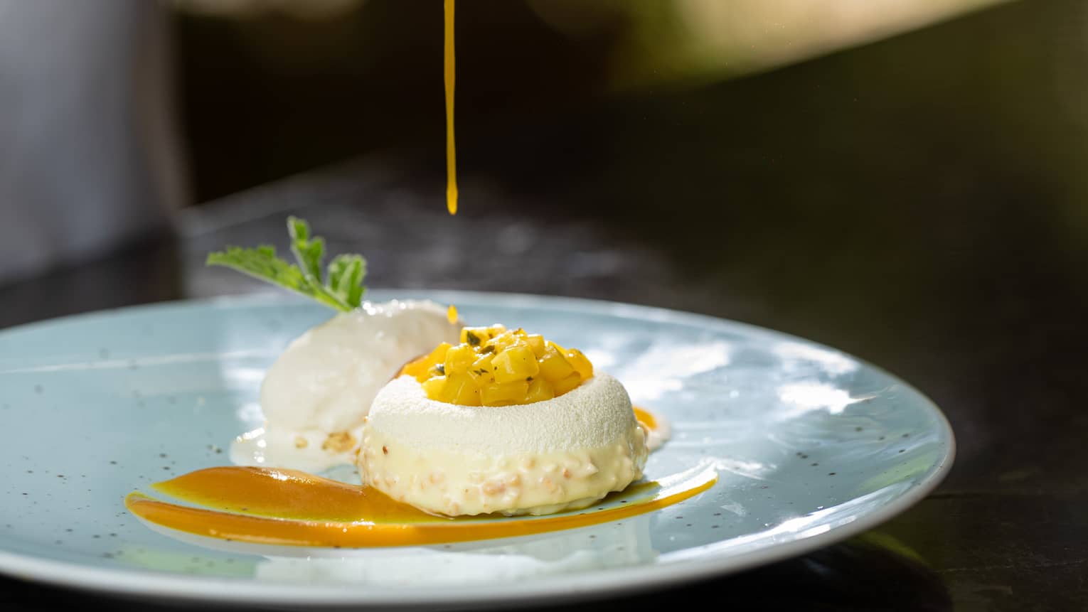 Coconut Dacquoise Biscuit Filled with Mango Mint Salsa Beside Coconut Sorbet with sauce being poured over