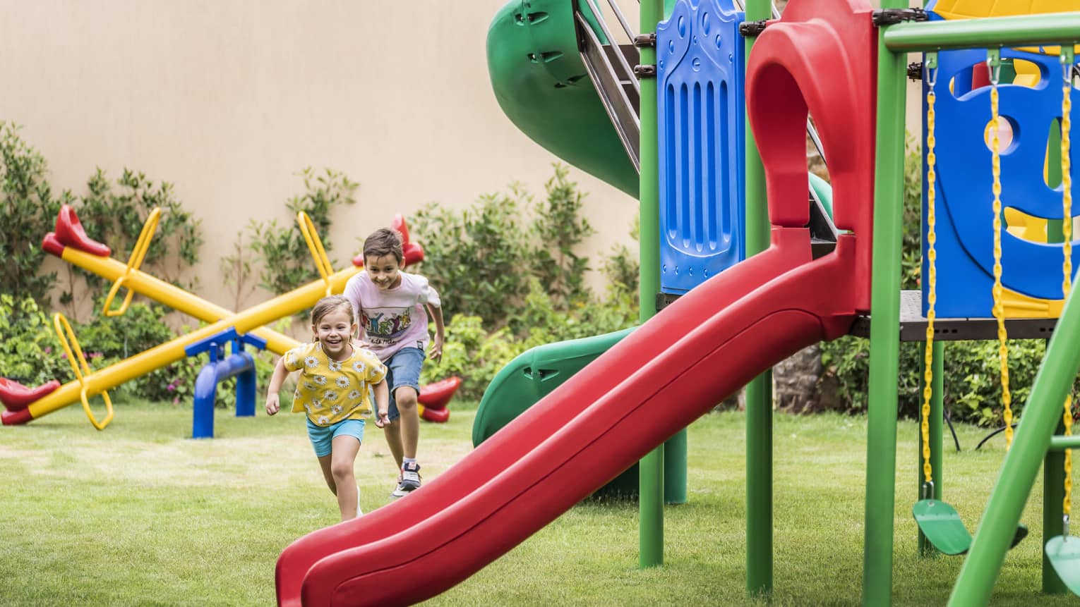 Two young boys run across a yard with playground equipment