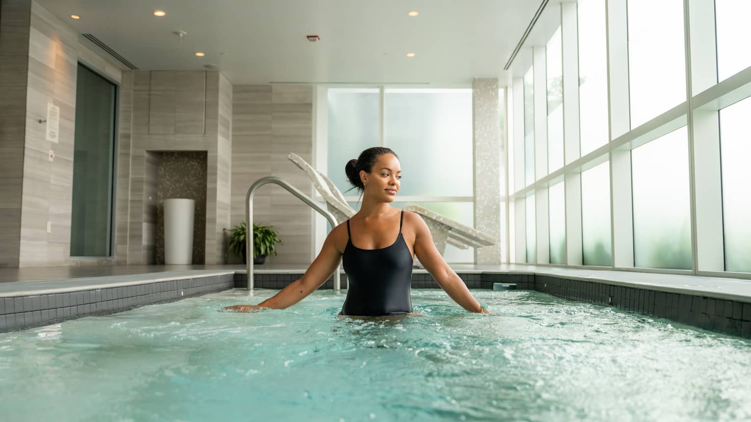 Guest wearing a swimsuit and standing in the pool in a room with floor-to-ceiling windows.