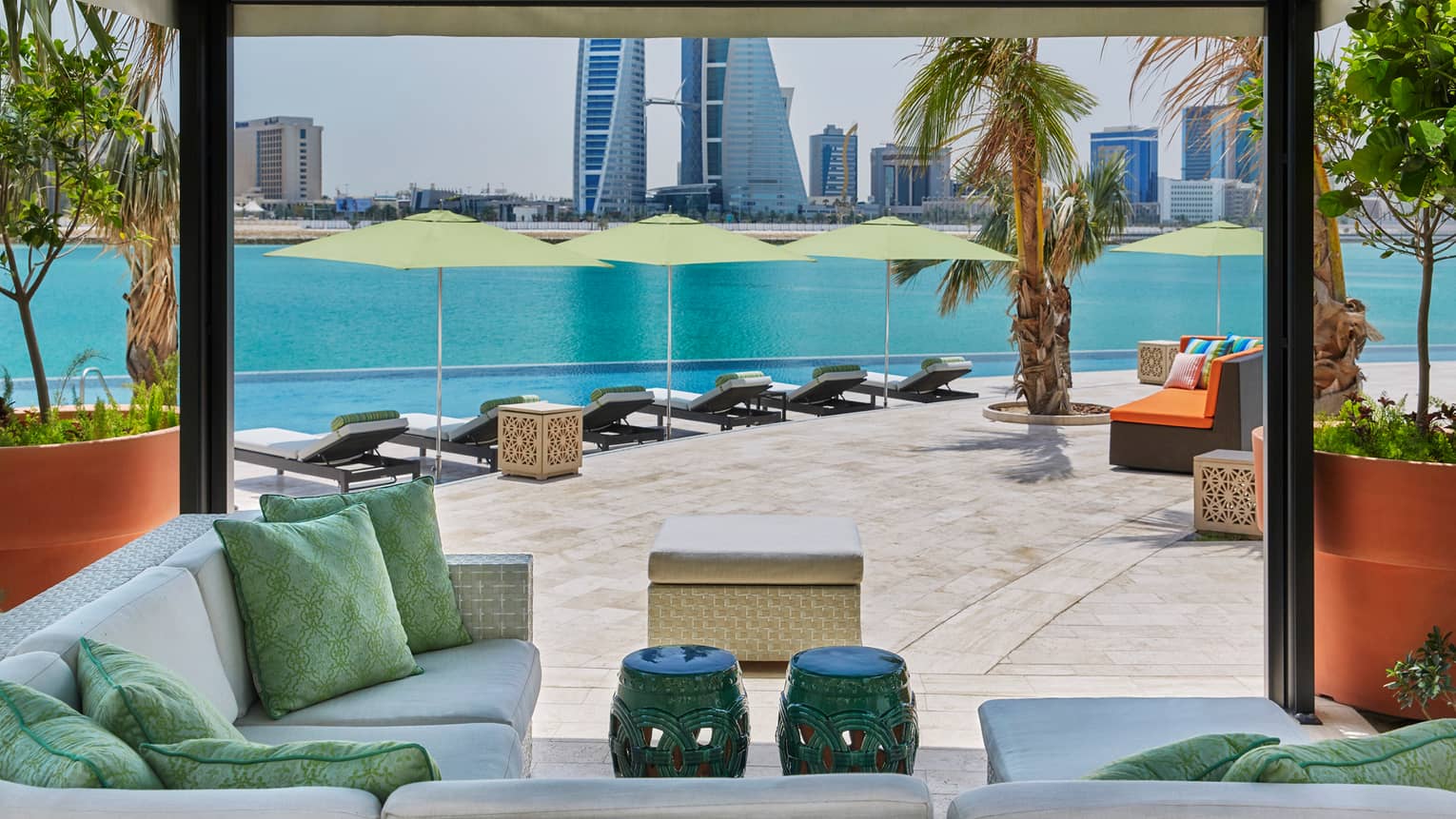 Plush outdoor patio seating and pillows under cabana, infinity swimming pool and Arabian Gulf in background