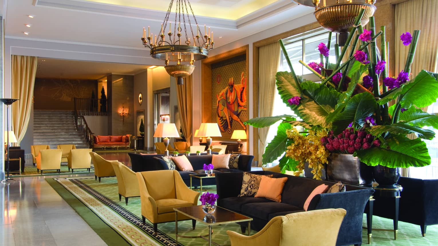 Sunny hotel lobby with blue sofas, yellow armchairs, large tropical plant with purple flowers