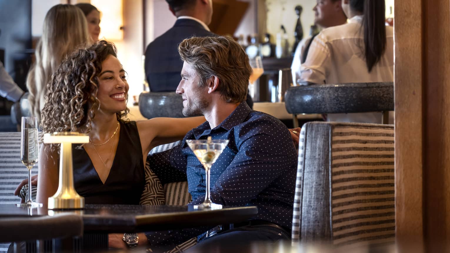 A group of people around a bar and sitting at a table conversing.