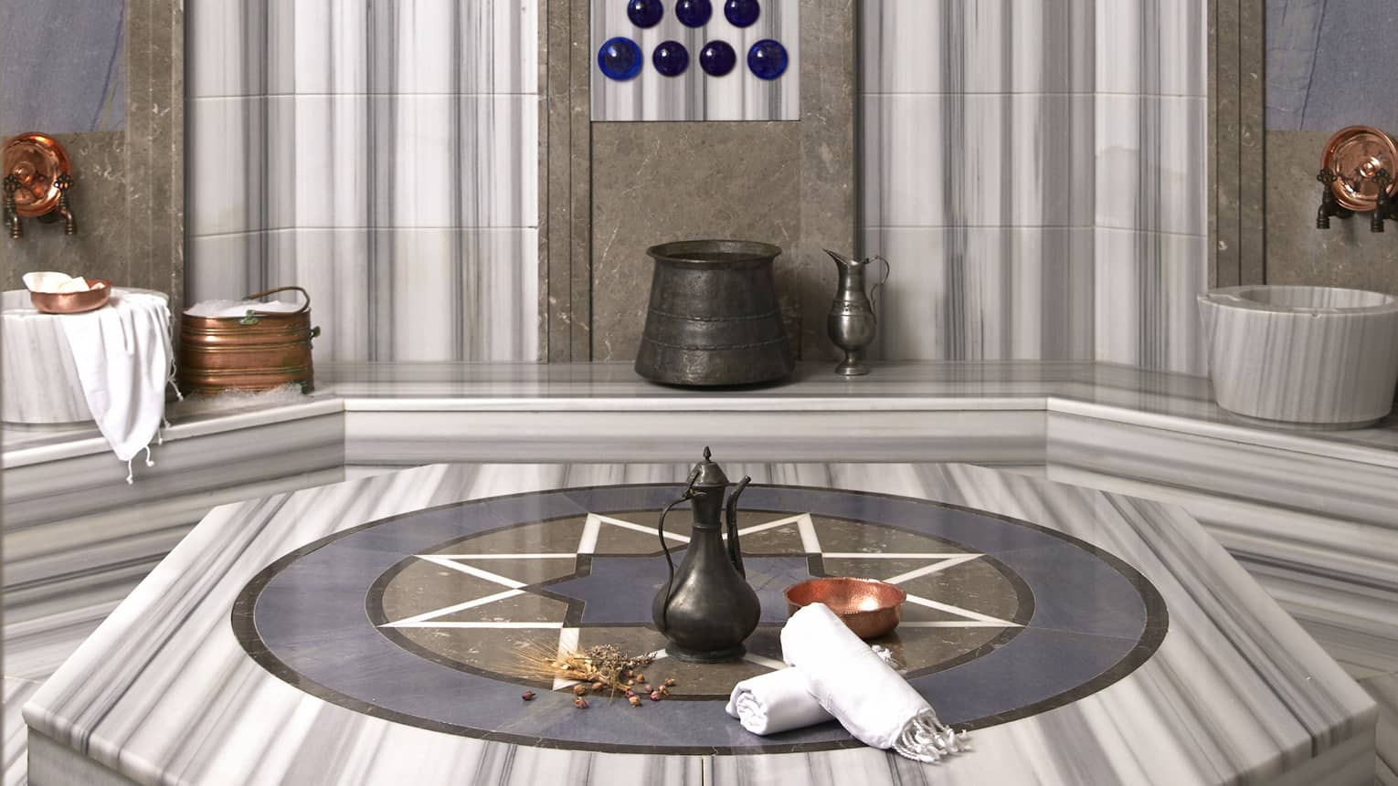 Rolled towels and kettle on marble bench in Turkish Hammam spa room