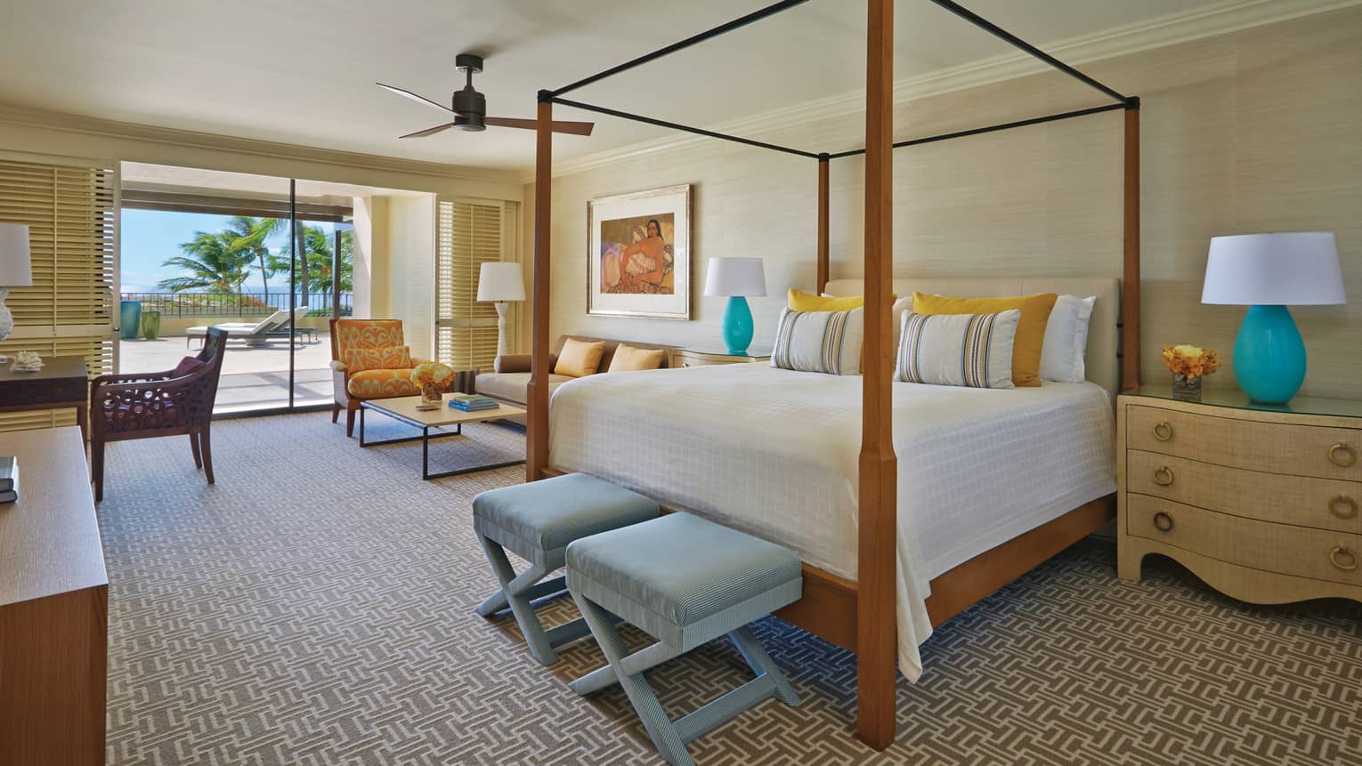 Bright bedroom with canopy bed, blue accents, desk, seating area and sliding doors leading to patio with palm trees