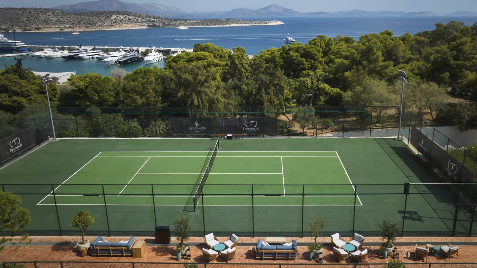 A tennis court with a forest and oceans in the background.