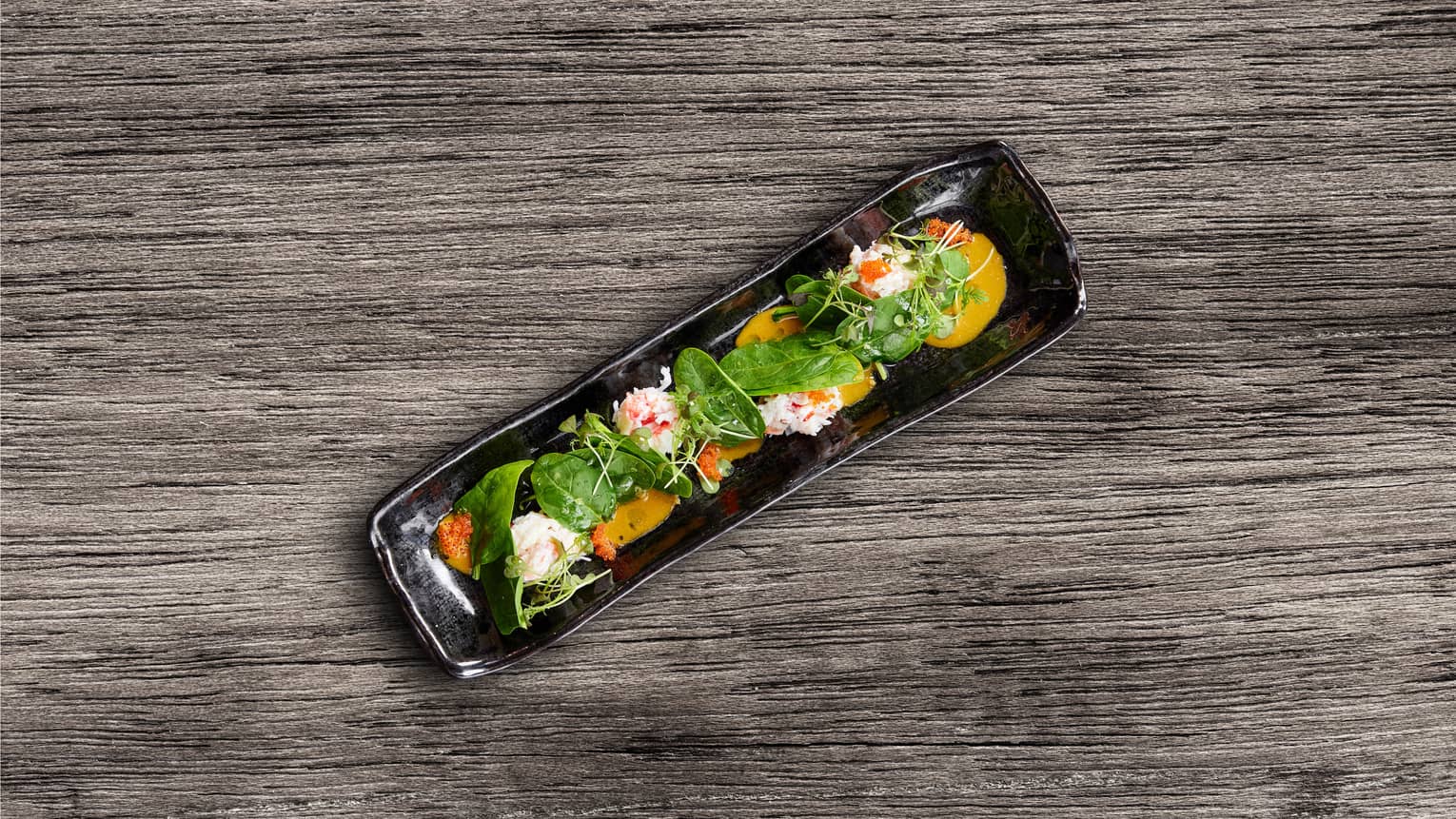 Crab and spinach salad on a rectangular black plate.