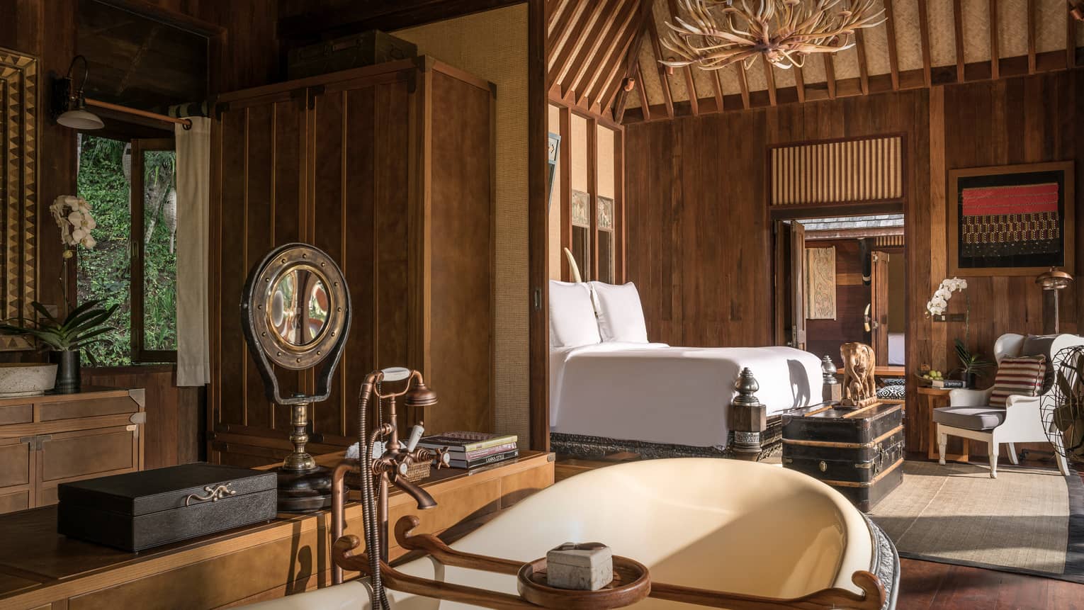 Two-bedroom Explorer's Lodge room with bed under rustic wood chandelier, large tub with brass faucet