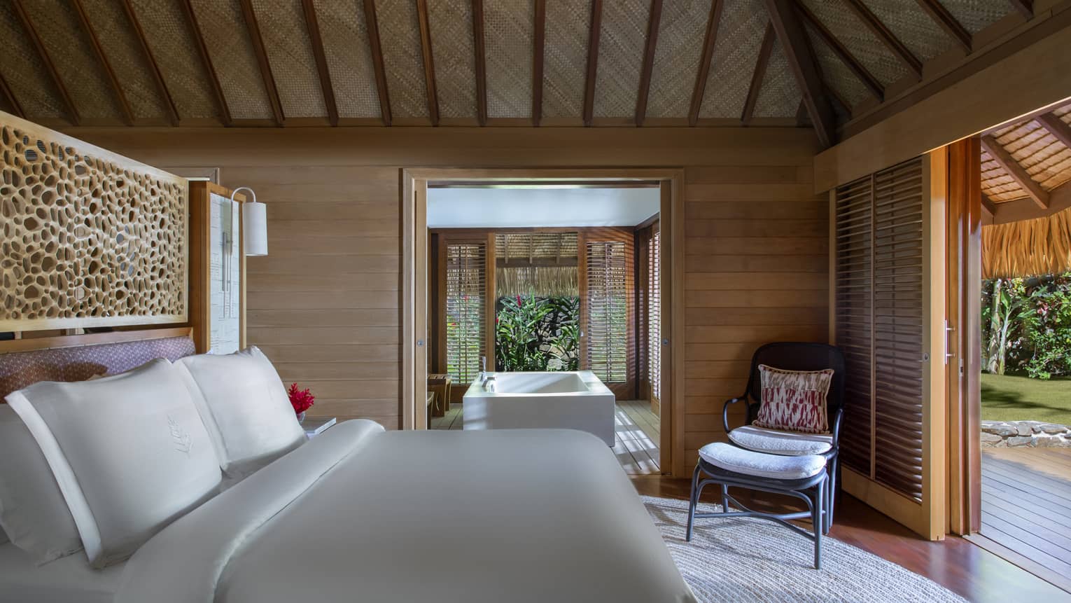 Bungalow villa bedroom with adjoining tub room, bed facing chair, open wall to patio