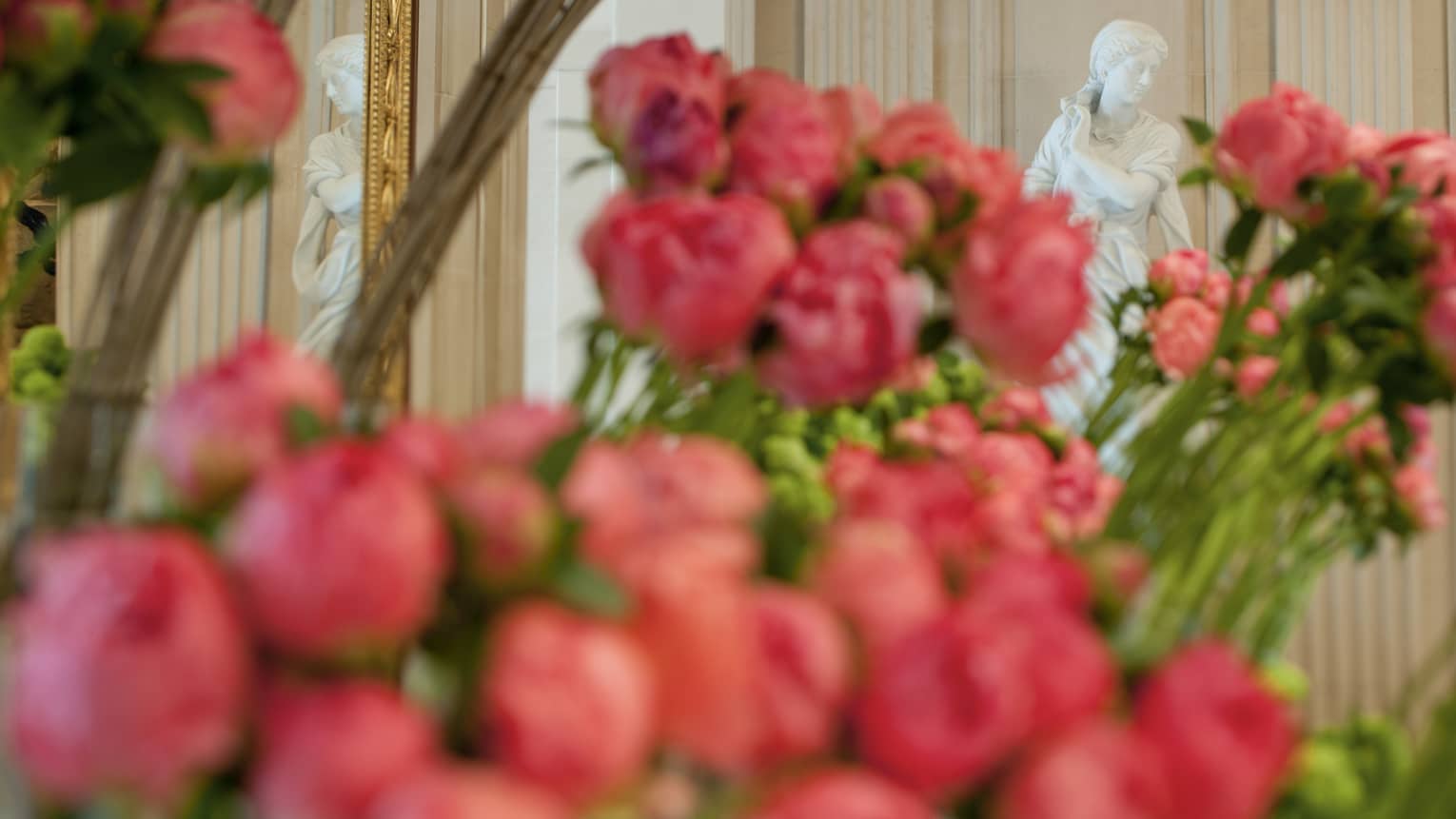 White statue behind bouquets of long stemmed pink roses