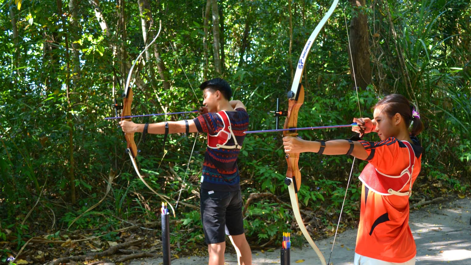 Man and woman stand with archery bow and arrows, prepare to shoot