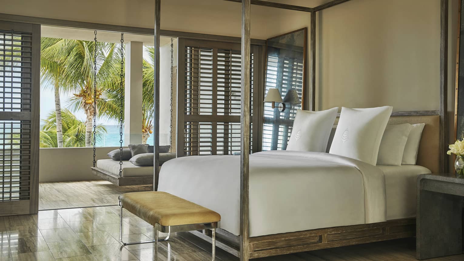 Elegant resort bedroom with a canopy bed, ocean-view balcony and hanging daybed.