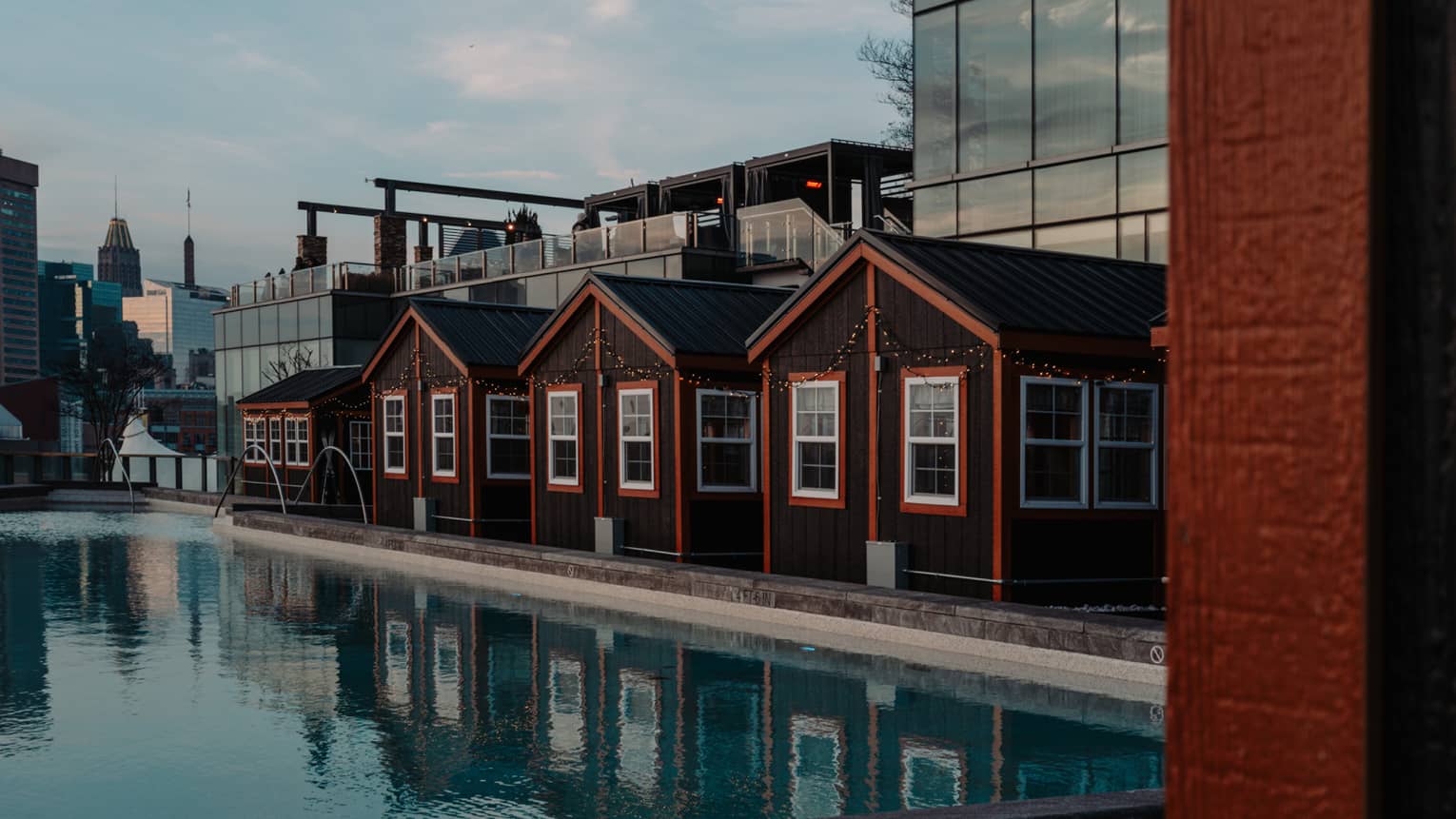 Four cottages with orange trimming beside a pool and city buildings